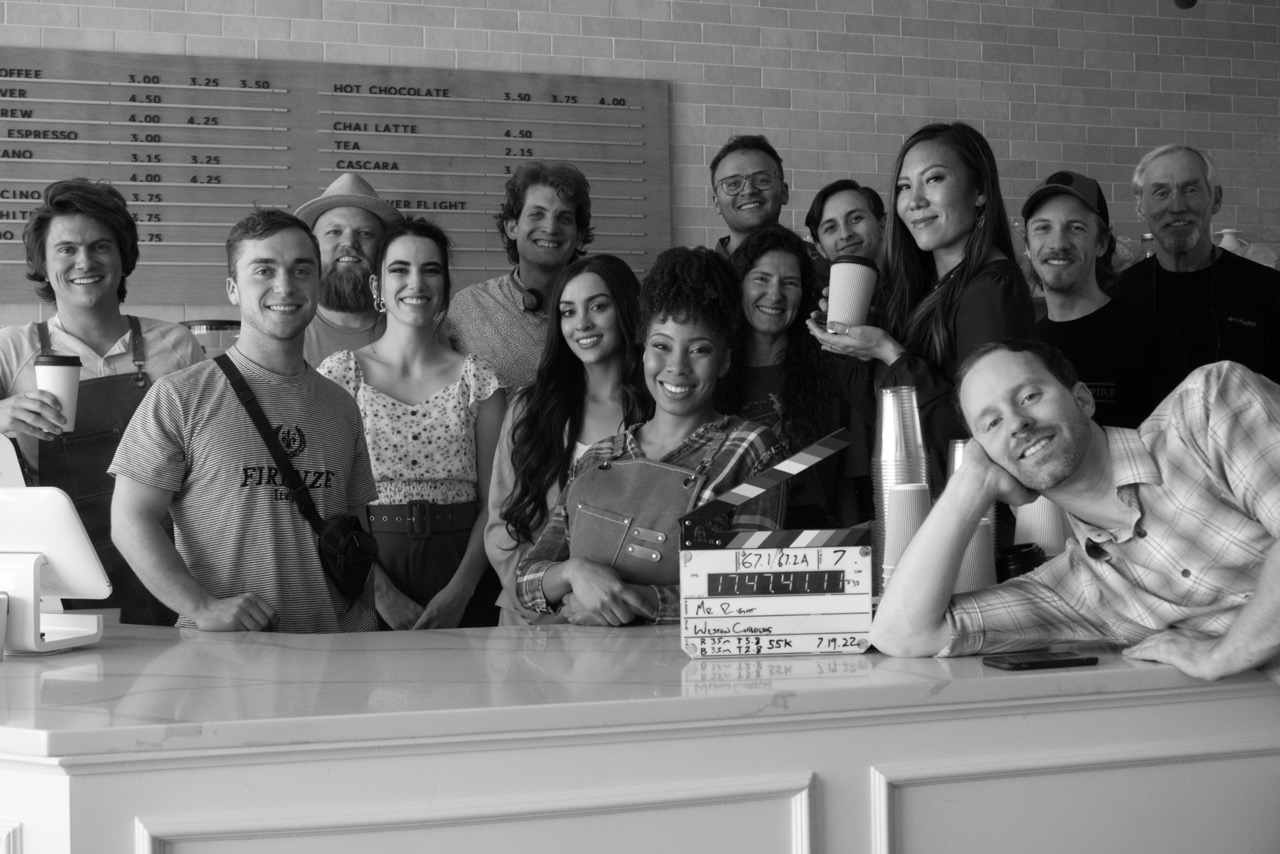A film cast and crew gathered around a counter on set